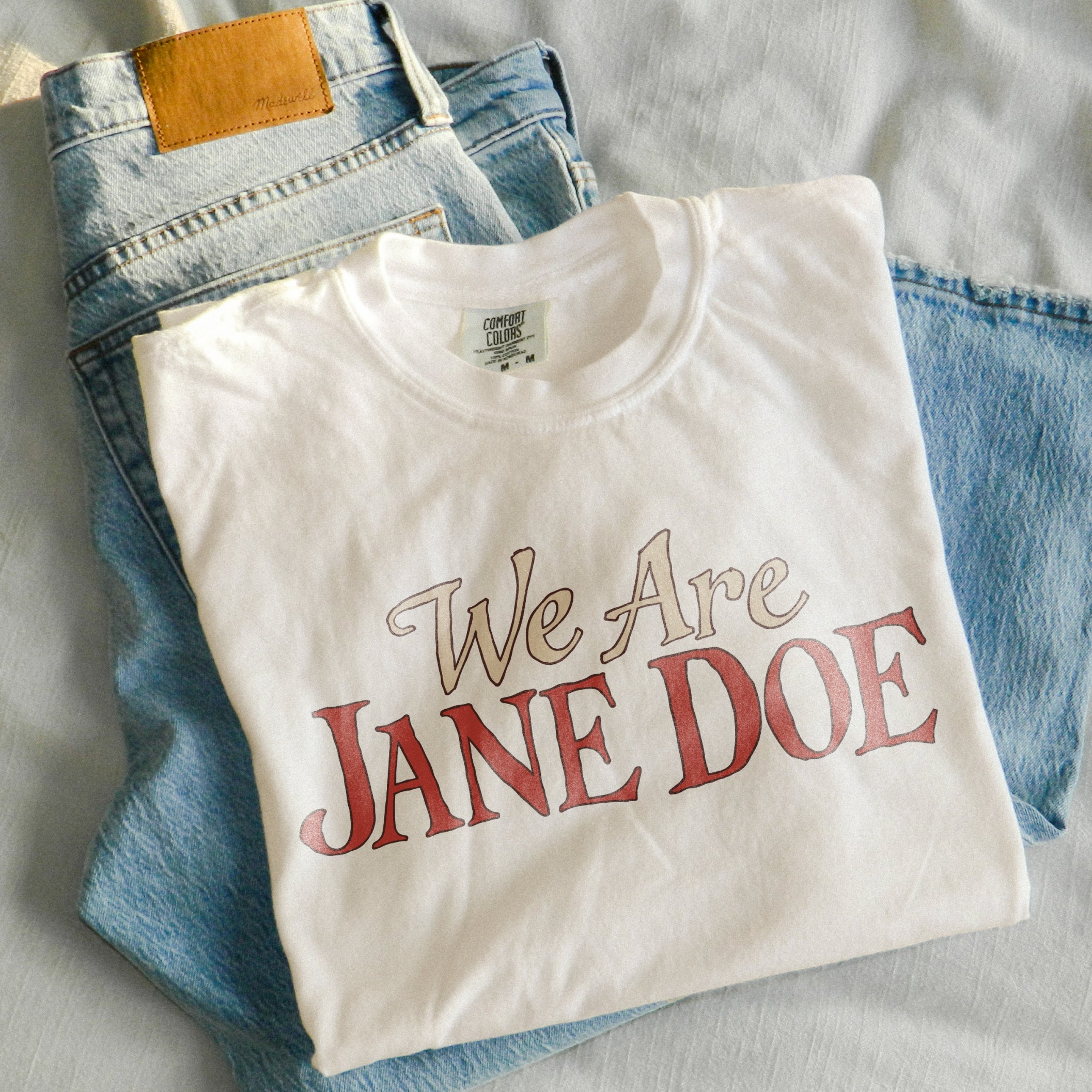 We are Jane Doe Tee in Ivory, folded on jeans